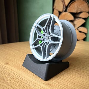 May include: A 3D printed model of a car wheel with a silver finish and a black base. The wheel has a detailed design with spokes and a brake rotor.