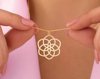 May include: A gold-colored pendant necklace featuring a floral design. The pendant is a symmetrical openwork pattern of overlapping circles. The necklace is held by a person, showcasing the delicate chain and the pendant's intricate details.