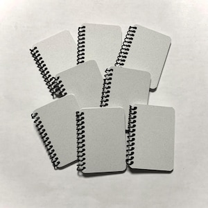 Puede incluir: Un montón de ocho pequeños cuadernos blancos de espiral con encuadernación de alambre negro.