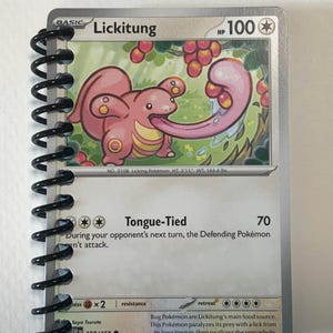 May include: A Lickitung Pokémon trading card, featuring a pink creature with a long tongue. The card has the text "Lickitung" and "Tongue-Tied". The card is bound with a black spiral binding.