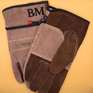 May include: A pair of brown leather work gloves. One glove features the initials "BM" in black, a red bead, and the brand name "HOZZA". The gloves have a black trim and are size 7.
