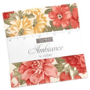 May include: A stack of square fabric swatches with pinked edges featuring a floral pattern in shades of red, yellow, and green on a cream background. A white paper band wraps around the centre, printed with the text Moda Fabrics Ambiance by 3 Sisters and a ruler measuring from 10 to 20 cm.