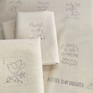 May include: A set of beige fabric panels with various embroidered designs, including a bee, a bird, a boat, a cat, and text that reads "bee happy", "Always in my", "rock the boat", "sleep in late sometime", and "A letter to my daughter".