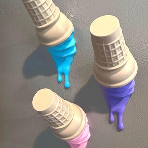 May include: Three whimsical ice cream cone magnets in a playful arrangement. Each cone features a beige waffle cone and a vibrant, drippy scoop of blue, purple, or pink ice cream. The magnets are designed to look like melting ice cream.