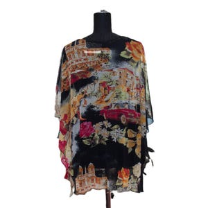 Op de afbeelding: Een zwarte poncho met een kleurrijke print van Italiaanse architectuur, een rode vintage cabriolet en diverse bloemmotieven, waaronder rozen. Het kledingstuk heeft een losvallend, vloeiend silhouet met wijde mouwen en een ronde hals.