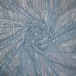 May include: A close-up of a light blue fabric with vertical, textured stripes. The fabric is swirled, creating a spiral pattern. The stripes are a lighter shade of blue, adding depth and dimension to the material.