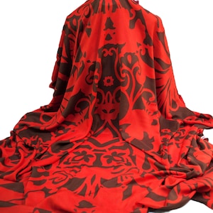 Könnte beinhalten: Ein roter Stoff mit einem sich wiederholenden braunen Blumenmuster. Der Stoff ist drapiert und erzeugt Falten und Schatten. Das Design zeigt stilisierte Blumen und wirbelnde Formen, geeignet für Heimdekoration oder Mode.