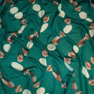 May include: Teal fabric featuring a repeating pattern of white ovals, geometric shapes in brown, black, and white, and white circles. The fabric has vertical stripes with a subtle metallic sheen. The fabric is draped, showing folds and shadows.