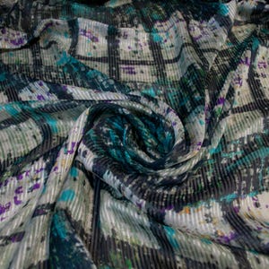 Puede incluir: Primer plano de una tela estampada con líneas entrecruzadas y salpicaduras de color. La tela presenta tonos turquesa, morado y gris, con un brillo sutil. El diseño tiene un aspecto moderno y abstracto.