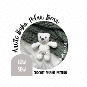 May include: A handmade white crochet polar bear plushie. The bear is positioned in front of a dark green knitted blanket. Text on the image reads "Arctic Bubs: Polar Bear" and "Crochet Plushie Pattern". A gray box reads "Low Sew".