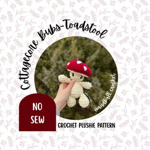 May include: A crocheted mushroom plushie with a red cap and white spots. The plushie is cream-colored and has a smiling face. The image includes the text "Cottagecore Bubs-Toadstool" and "NO SEW CROCHET PLUSHI PATTERN".