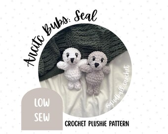 May include: Two crocheted seal plushies, one white and one gray, are displayed. The image includes text that reads "Arctic Bubs. Seal" and "Crochet Plushie Pattern." The design also features the words "Low Sew."