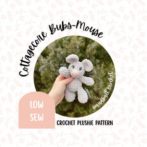May include: A gray crochet mouse plushie with a pink nose and black eyes is held in a hand. The image includes the text "Cottagecore Bubs-Mouse" and "Crochet Plushie Pattern". The background is a blurred green.
