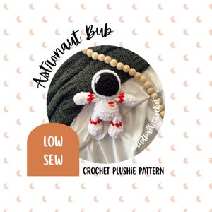 May include: A white and red crochet astronaut plushie with a black helmet. The image includes the text "Astronaut Bub", "LOW SEW", and "CROCHET PLUSHIE PATTERN". The plushie is lying on a white surface with a green blanket in the background.