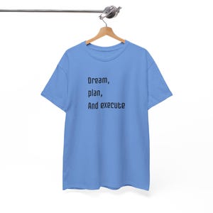 Puede incluir: Una camiseta azul claro con el texto "Dream, plan, And execute" impreso en negro.