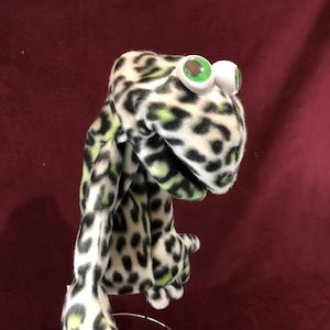 May include: A hand puppet with a white and black leopard print fabric. The puppet has green eyes and a wide open mouth.
