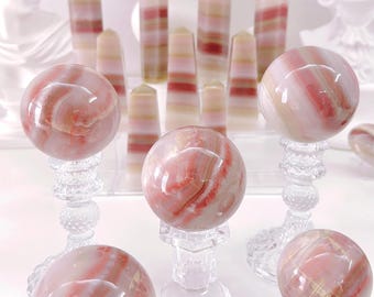May include: A collection of pink and white striped crystal spheres on clear glass stands. The spheres are arranged in a semi-circle on a white surface.