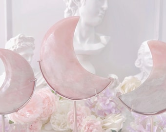 May include: Three pink crescent moon shaped crystals on metal stands. The crystals are translucent and have a white and pink marbled appearance. The crystals are arranged in a row from largest to smallest.