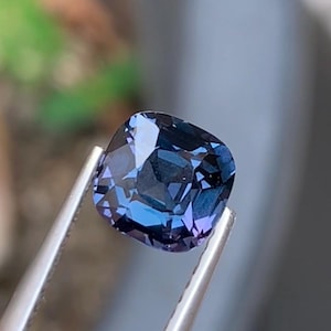 Könnte beinhalten: Ein Edelstein im Kissenschliff mit einer tiefblauen und violetten Farbpalette. Der Stein hat eine facettierte Oberfläche, die das Licht reflektiert und deutliche dunkel- und hellblaue Töne auf seiner quadratischen Form mit abgerundeten Ecken erzeugt.