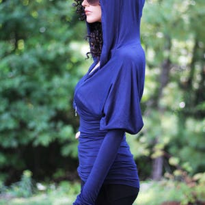 May include: A blue hooded top with long sleeves and a fitted silhouette. The top has a zipper closure and a relaxed fit.