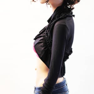May include: A black cropped shrug with a ruffled neckline and long sleeves.