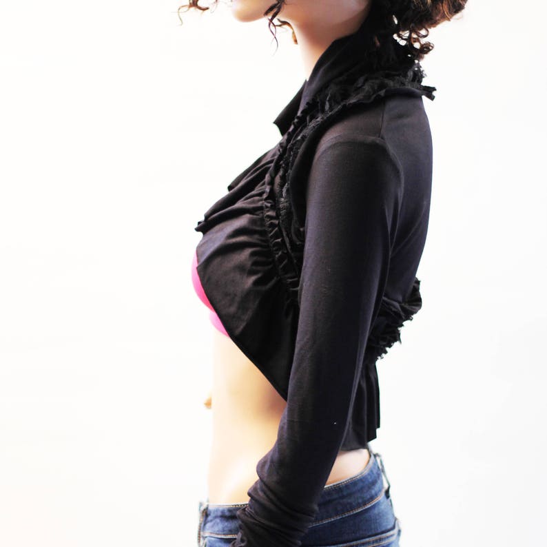 May include: A black cropped shrug with a ruffled neckline and long sleeves.