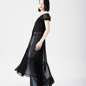 May include: A black sheer maxi dress with a ruffled hem and short sleeves. The dress is worn over a pair of blue jeans.