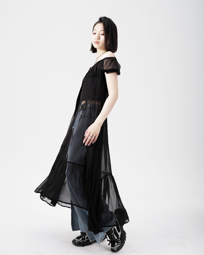 May include: A black sheer maxi dress with a ruffled hem and short sleeves. The dress is worn over a pair of blue jeans.
