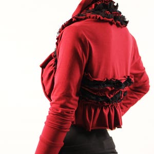 May include: A maroon long-sleeved shrug with black lace trim and ruffles. The shrug has a high neckline and a cropped length.