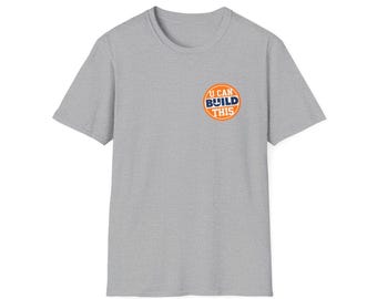 May include: A heather gray t-shirt with a crew neck and short sleeves. The shirt features a circular graphic on the left chest that reads "I CAN BUILD THIS" in blue and white text on an orange background.