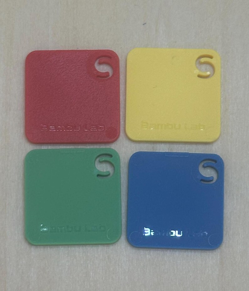 May include: Four square plastic samples in red, yellow, green, and blue. Each sample has a small "S" cut out of the top right corner and the text "Bamboo Lab" printed on the bottom.