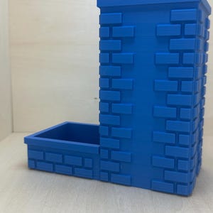 May include: A blue 3D printed dice tower with a brick pattern. The tower has a separate compartment for dice.