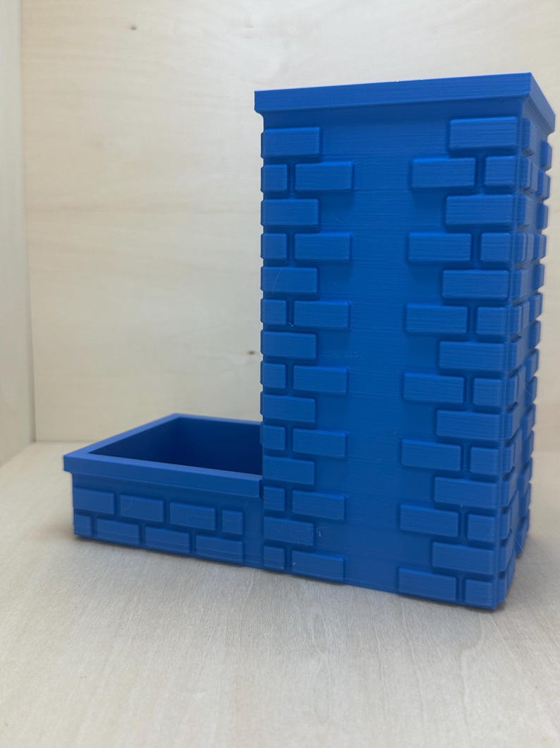 May include: A blue 3D printed dice tower with a brick pattern. The tower has a separate compartment for dice.