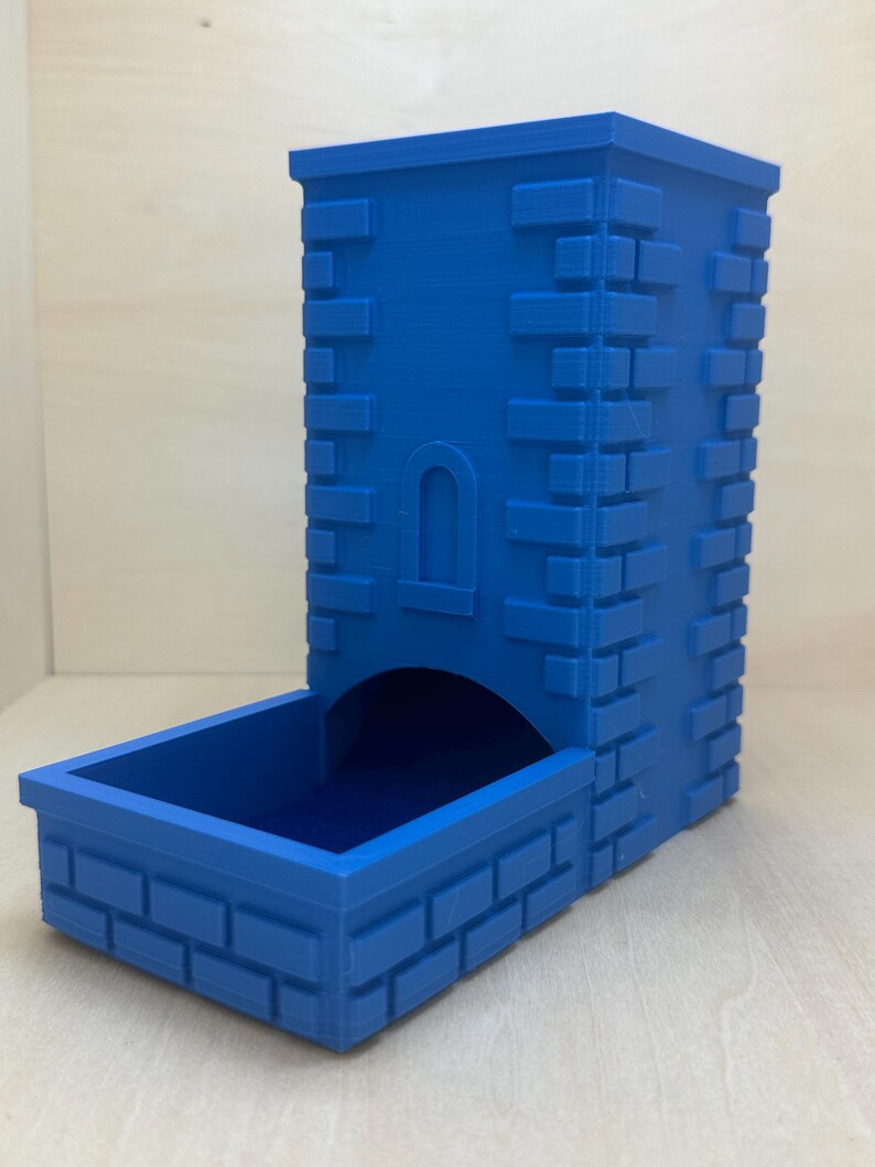 May include: A blue 3D printed dice tower shaped like a small castle with a brick pattern. The tower has a slot for dice to roll out of.