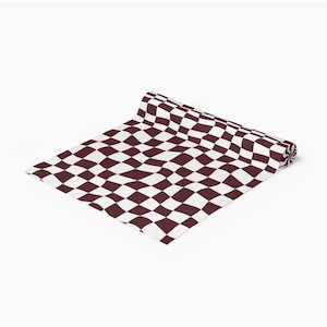 May include: A rolled up table runner with a checkered pattern in white and burgundy.