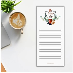 May include: White notepad with a black and white illustration of a football, a cooler, and a bow tie. The illustration is surrounded by green leaves and the text "Tailgate Time".