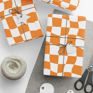May include: Orange and white checkered wrapping paper with a wavy pattern. The paper is tied with brown twine and has a white star and heart shaped tag.