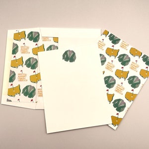 May include: A set of three white stationery cards with a repeating pattern of green golf jackets and yellow golf courses with red flags. The cards are blank and ready for writing.