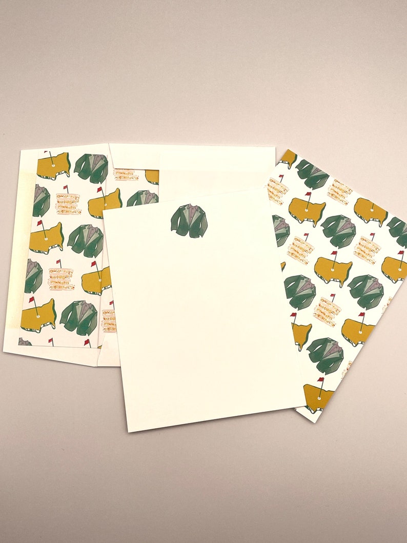 May include: A set of three white stationery cards with a repeating pattern of green golf jackets and yellow golf courses with red flags. The cards are blank and ready for writing.