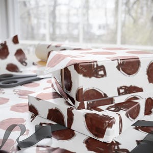 May include: White gift wrap with a brown football helmet pattern. The gift wrap is wrapped around a box and there is a black ribbon on the table.