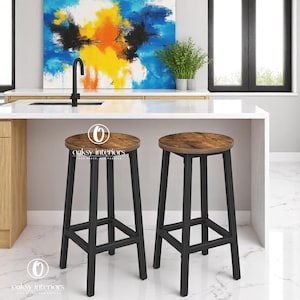 May include: Two bar stools with a rustic wood-effect seat and black metal frame. The stools are in a kitchen setting with a white countertop and abstract art in the background. The stools have the text "Oaksy Interiors" on them.