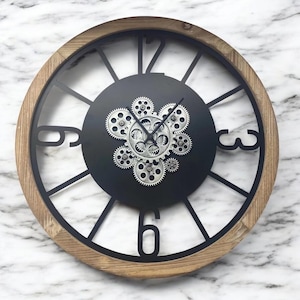 May include: A large, round wall clock with a wooden frame and black metal accents. The clock face features a black background with silver gears and Roman numeral hour markers.