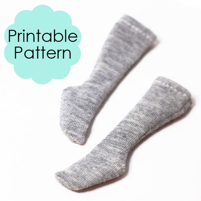 K&ouml;nnte beinhalten: Ein Paar graue gestrickte Puppensocken. Die Socken sind lang und haben eine gerippte Struktur. Die Socken liegen auf einem wei&szlig;en Hintergrund. Druckbarer Schnittmuster.