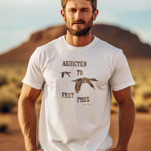 May include: White t-shirt with a camouflage print of ducks and the text "Addicted to Fast Food".