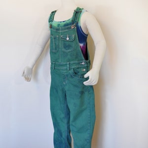 Può includere: Salopette di jeans verde con un top a fascia tie-dye sotto. La salopette ha una singola tasca anteriore e bretelle regolabili.