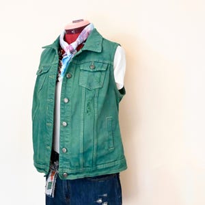 Op de afbeelding: Een groene denim vest met een wit T-shirt eronder en blauwe denim shorts. De vest heeft een knoopsluiting en meerdere zakken. De shorts hebben distressed details.