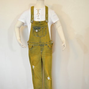 May include: Yellow denim overalls with a white lace-up top. The overalls have a front pocket and distressed details.
