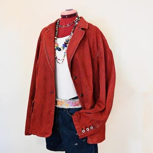 May include: A red blazer with a white tank top, denim shorts, and a colorful belt. The outfit is accessorized with beaded necklaces. The blazer has buttoned cuffs and a classic lapel.