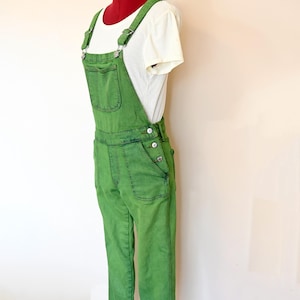 Op de afbeelding: Groene denim overall met een wit T-shirt eronder. De overall heeft verstelbare banden en een enkele voorzak.