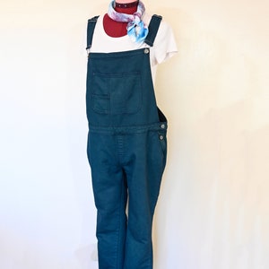 Op de afbeelding: Teal blauwe denim overall met een wit T-shirt en een blauwe en rode gestreepte sjaal.